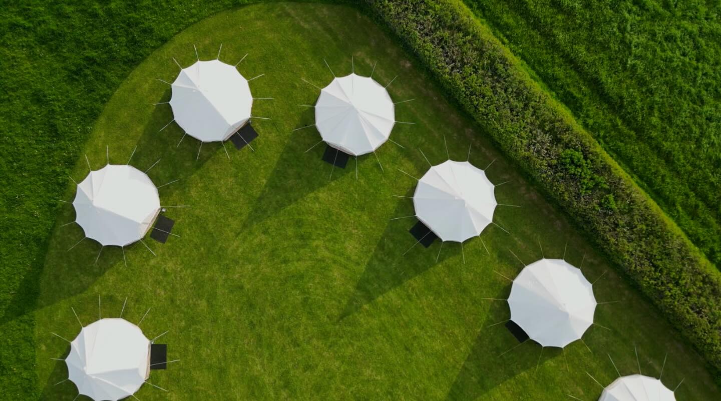 Aerial view of seven white bell tents arranged in a curve on a green lawn